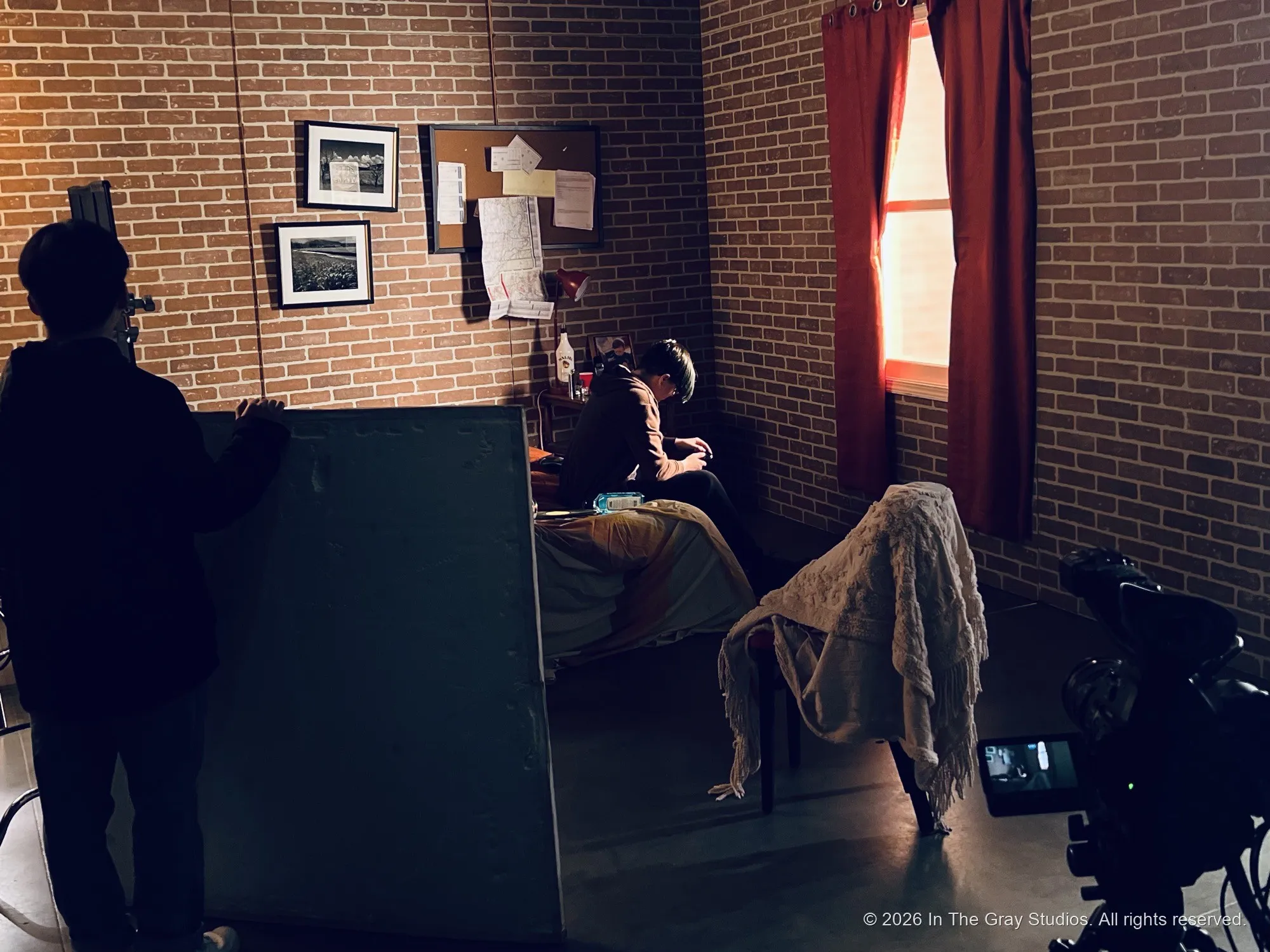 A crew member silhouetted against a lit set dressed as a bedroom