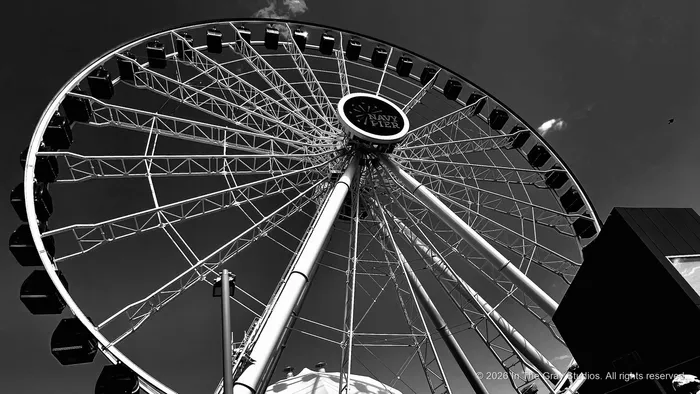 A ferris wheel in black and white, spokes radiating against a bright sky
