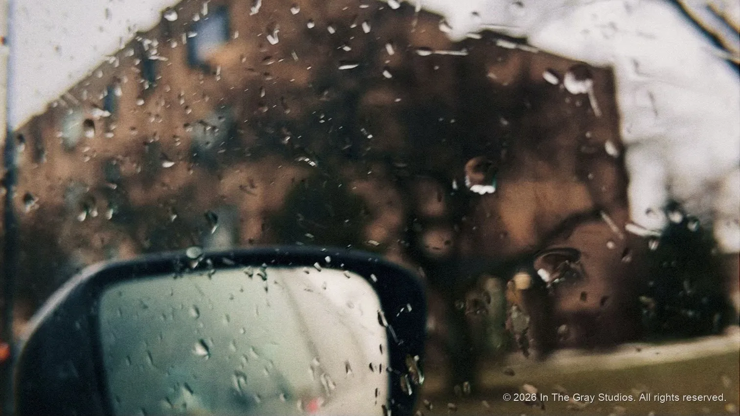 Rain beading on a car window, a side mirror soft in the blur beyond