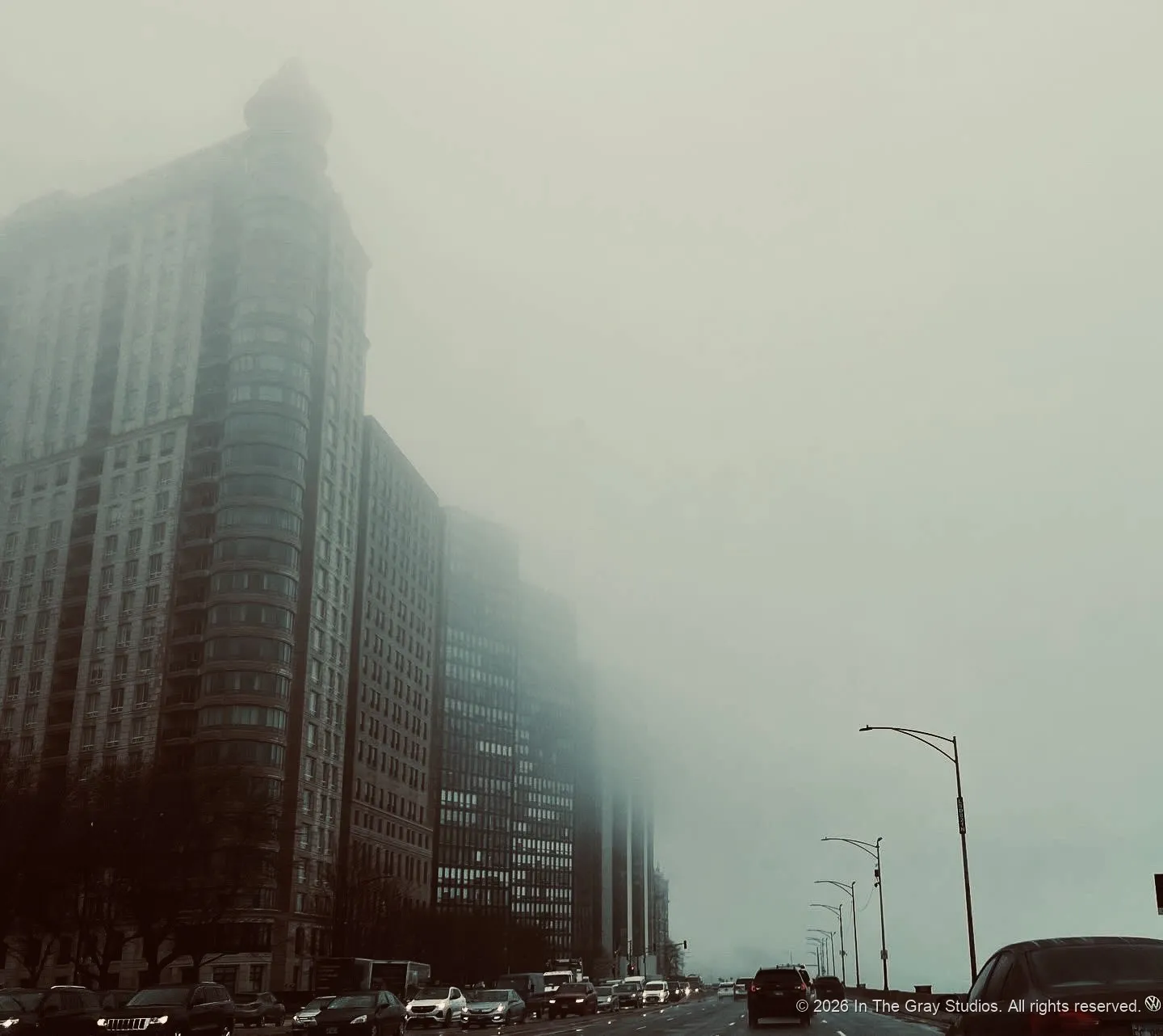 A high-rise dissolving into fog above a grey street